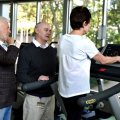 Two people stand next to a person walking on a treadmill